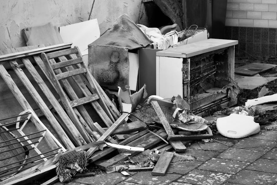 A narrow urban alleyway filled with a large collection of mixed waste and debris, including black plastic bags, cardboard boxes, and assorted rubbish piled high at the far end of the alley. In the for